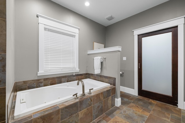 bathroom with stone finish floors, a jetted tub, and baseboards