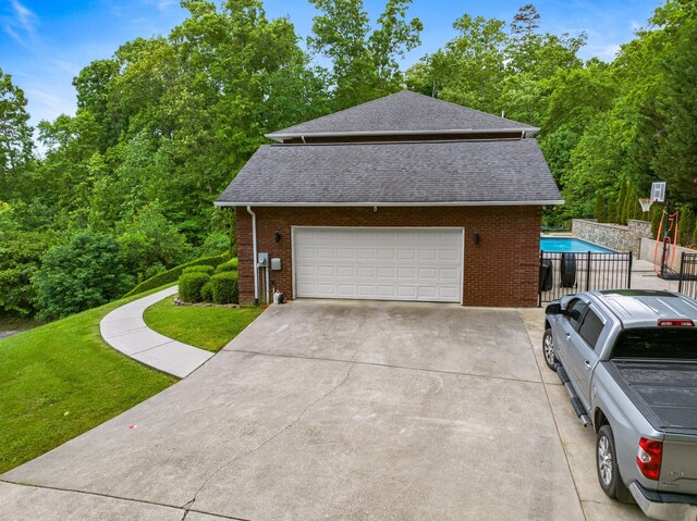 view of home's exterior with a garage, a shingled roof, brick siding, concrete driveway, and an outdoor pool