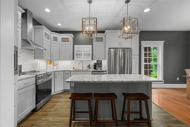 kitchen featuring stainless steel appliances, wall chimney range hood, a sink, a breakfast bar area, and a chandelier