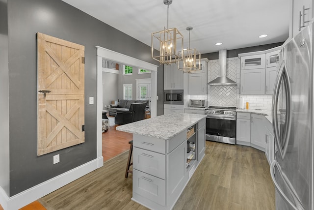 kitchen featuring stainless steel appliances, wall chimney range hood, a chandelier, light wood-style flooring, and backsplash