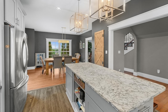kitchen with freestanding refrigerator, a chandelier, dark wood-type flooring, a kitchen island, and baseboards