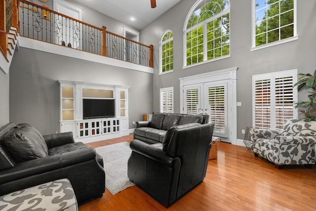 living area featuring a towering ceiling, wood finished floors, french doors, ceiling fan, and baseboards