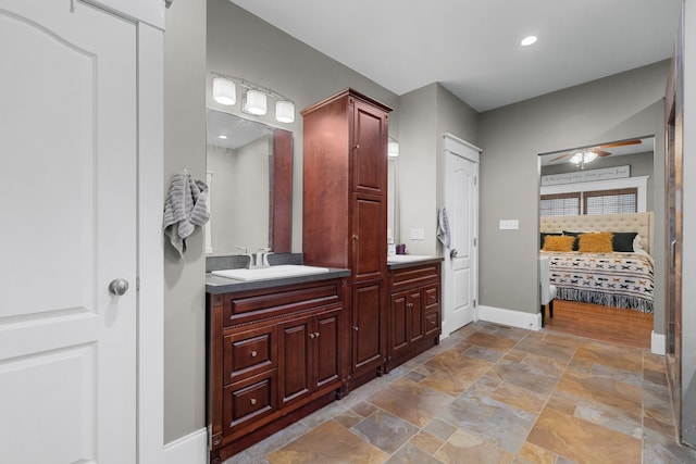 ensuite bathroom with stone finish flooring, ceiling fan, baseboards, and vanity