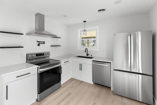 kitchen with wall chimney range hood, sink, appliances with stainless steel finishes, white cabinetry, and hanging light fixtures