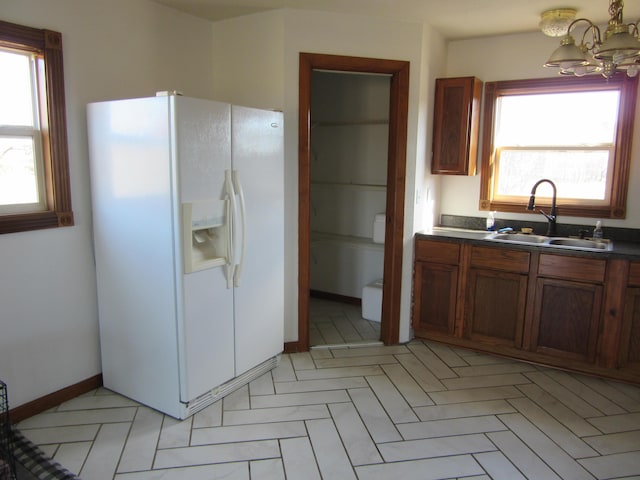 kitchen with plenty of natural light, dark countertops, white refrigerator with ice dispenser, and a sink