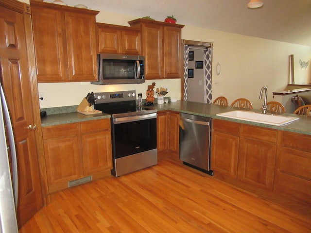 kitchen featuring stainless steel appliances, a sink, visible vents, light wood-style floors, and brown cabinetry