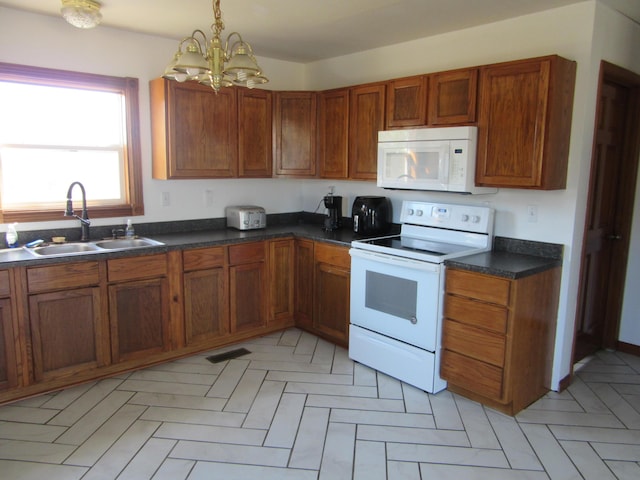 kitchen featuring brown cabinets, decorative light fixtures, dark countertops, a sink, and white appliances