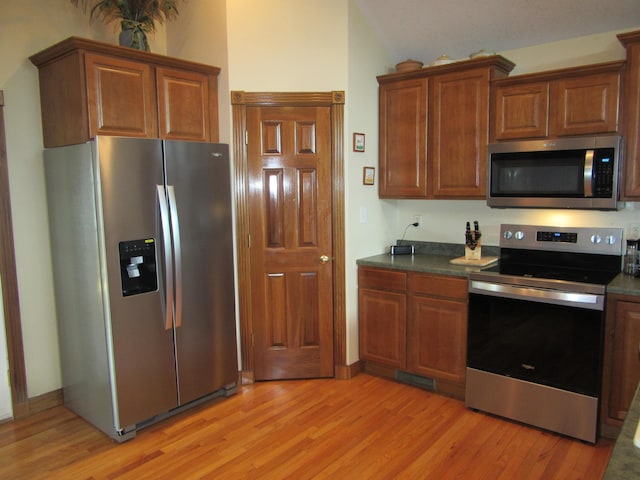 kitchen featuring dark countertops, light wood-style floors, stainless steel appliances, and brown cabinetry