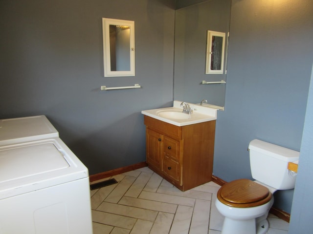 half bath featuring washing machine and clothes dryer, visible vents, toilet, vanity, and baseboards