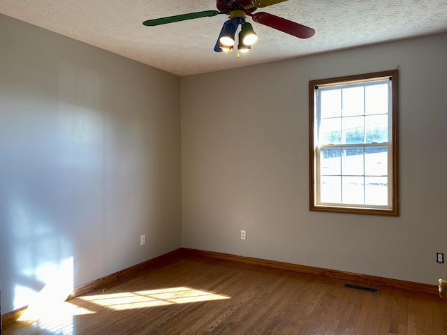 empty room with ceiling fan, wood-type flooring, and a textured ceiling