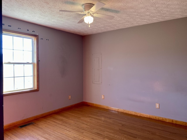 unfurnished room featuring hardwood / wood-style flooring, ceiling fan, electric panel, and a textured ceiling