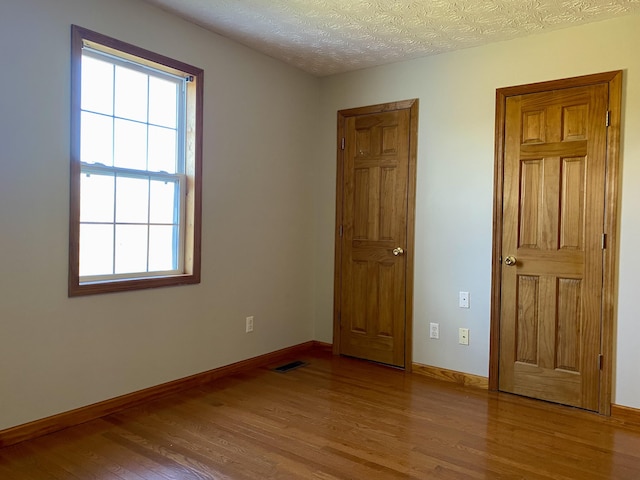 unfurnished bedroom featuring multiple windows, light hardwood / wood-style flooring, and a textured ceiling