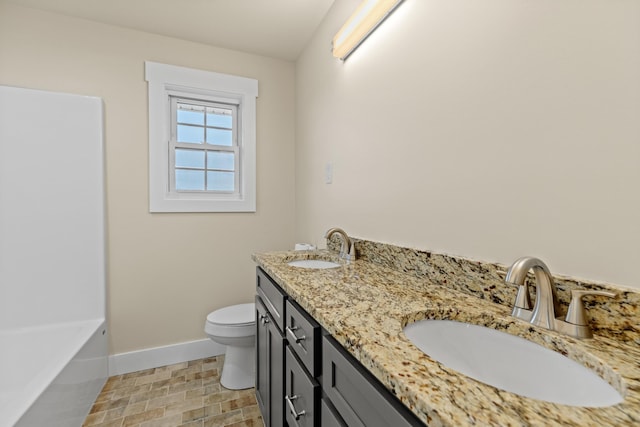 full bathroom with baseboards, double vanity, a sink, and toilet