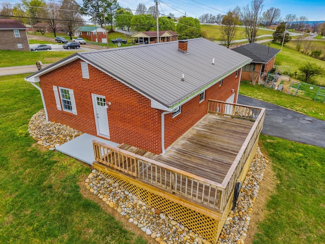 back of property with a chimney, a deck, brick siding, a residential view, and a yard