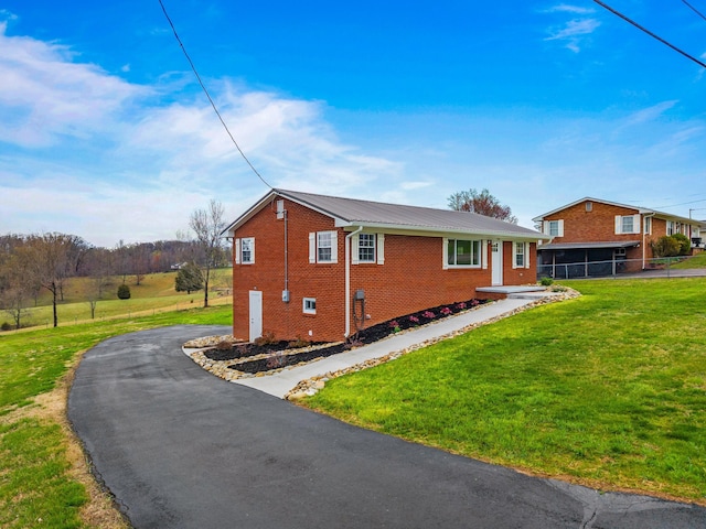 view of side of property with driveway, fence, brick siding, metal roof, and a yard