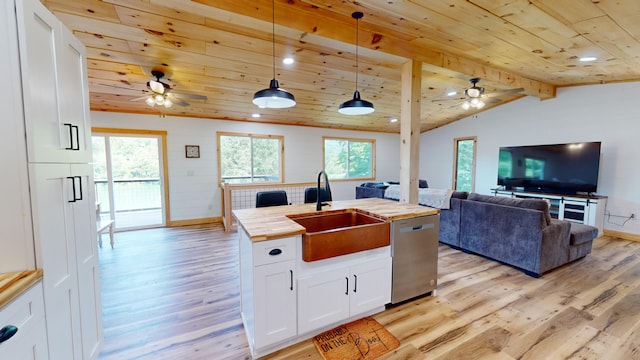 kitchen with wood counters, stainless steel dishwasher, pendant lighting, white cabinetry, and an island with sink