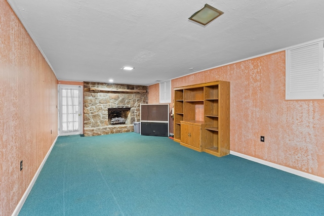 unfurnished living room featuring a stone fireplace, wood walls, crown molding, carpet floors, and a textured ceiling