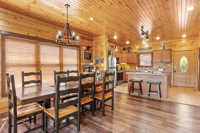 dining area with an inviting chandelier, light hardwood / wood-style flooring, wooden ceiling, and wooden walls