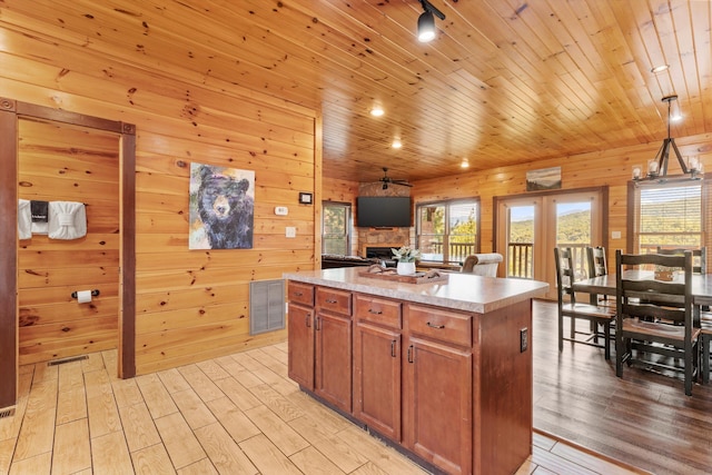 kitchen featuring pendant lighting, wood ceiling, light hardwood / wood-style flooring, a center island, and a stone fireplace