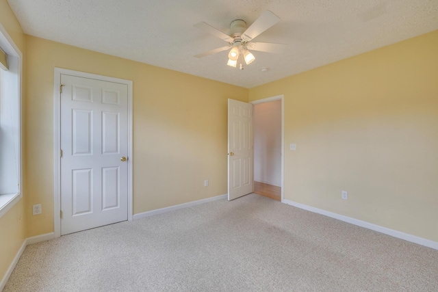 unfurnished bedroom featuring ceiling fan, light carpet, and a textured ceiling