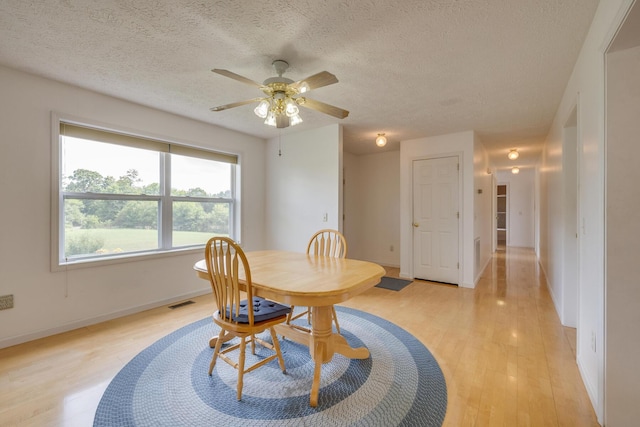 dining space with ceiling fan, a textured ceiling, and light hardwood / wood-style floors