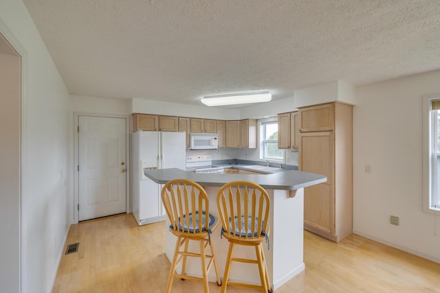 kitchen with sink, a breakfast bar area, light wood-type flooring, a kitchen island, and white appliances