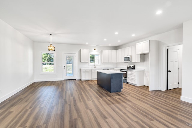 kitchen with appliances with stainless steel finishes, dark hardwood / wood-style flooring, a kitchen island, decorative light fixtures, and white cabinetry