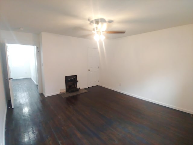 empty room with dark hardwood / wood-style floors, ceiling fan, and a wood stove