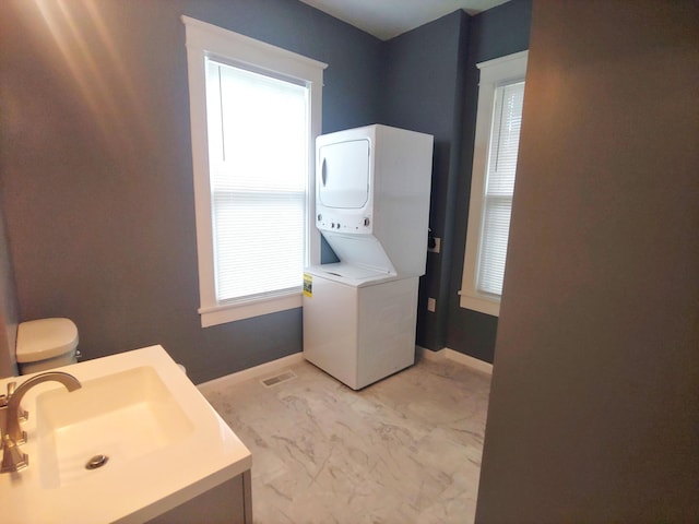 bathroom featuring a healthy amount of sunlight, sink, and stacked washer / dryer