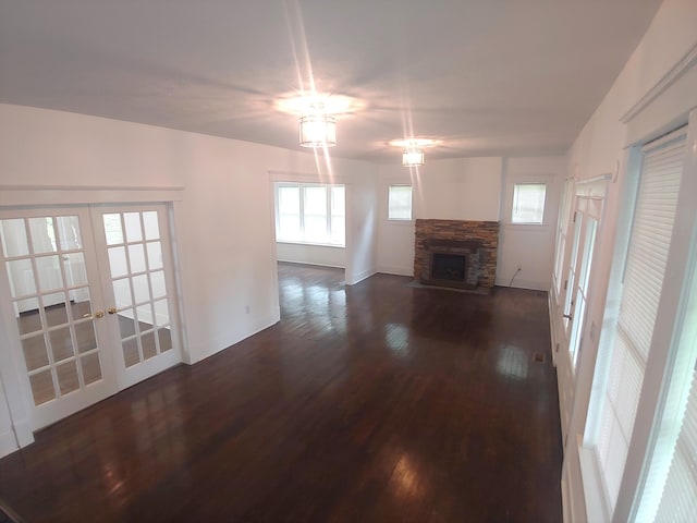 unfurnished living room with french doors, a stone fireplace, and dark wood-type flooring