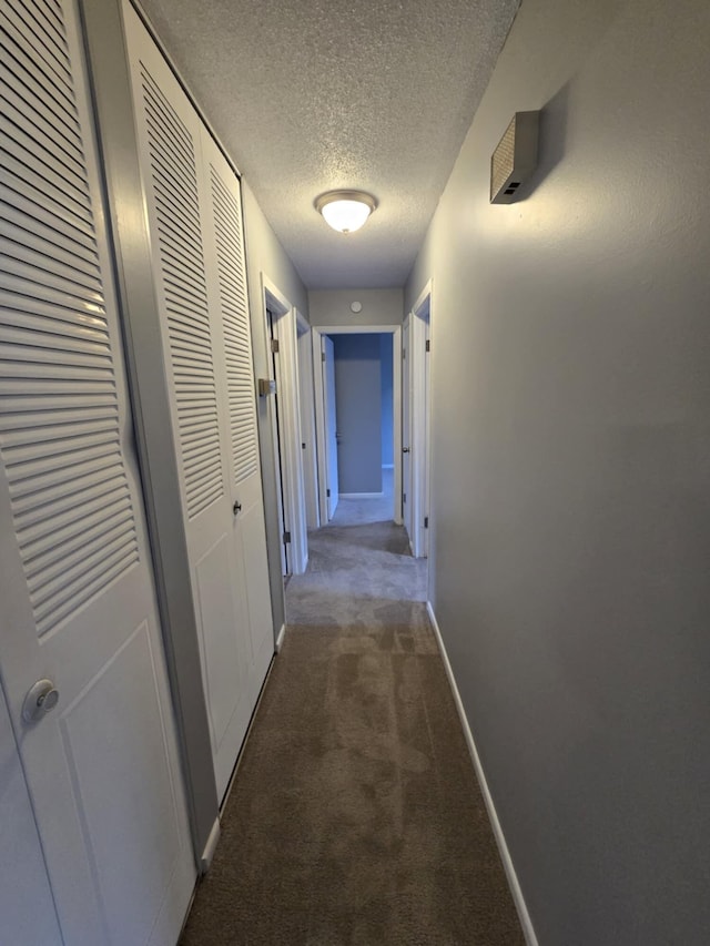 corridor with a textured ceiling and dark carpet