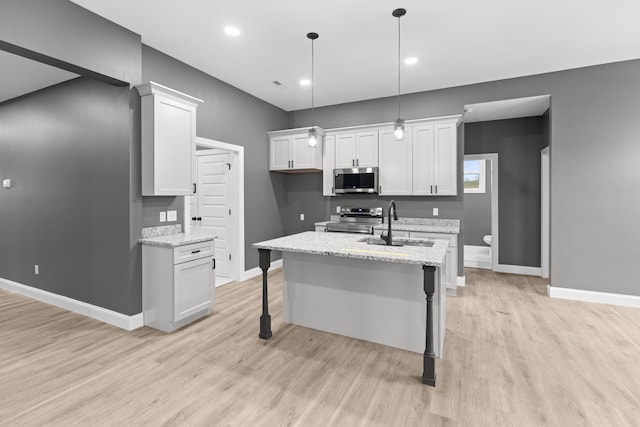 kitchen with hanging light fixtures, light stone counters, a kitchen island with sink, white cabinets, and appliances with stainless steel finishes