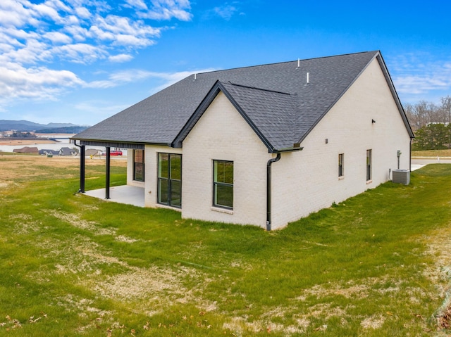 rear view of house with a mountain view, a patio, central AC unit, and a lawn