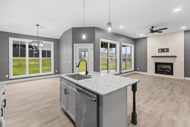 kitchen with dishwasher, a kitchen island with sink, hanging light fixtures, sink, and light stone counters