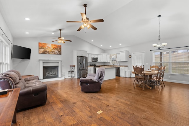 living room featuring light wood-type flooring, ceiling fan with notable chandelier, and high vaulted ceiling