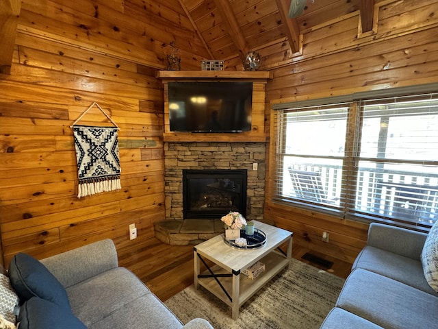 living area with vaulted ceiling with beams, a stone fireplace, wooden ceiling, wood walls, and wood finished floors