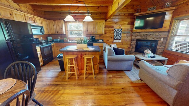 living room featuring lofted ceiling with beams, wood walls, a stone fireplace, wooden ceiling, and wood finished floors