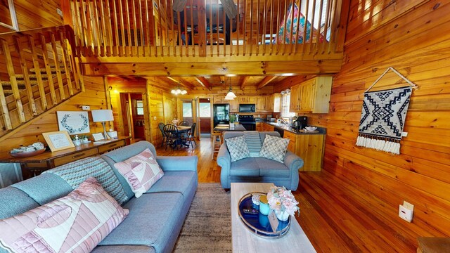 living area featuring light wood-type flooring, wood walls, stairway, and beamed ceiling