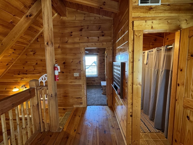 hall featuring lofted ceiling with beams, wood walls, wood-type flooring, and visible vents