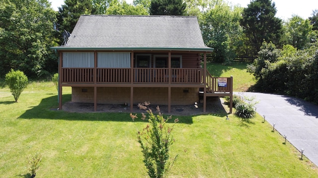 view of front of property with a deck, log exterior, a front yard, and roof with shingles