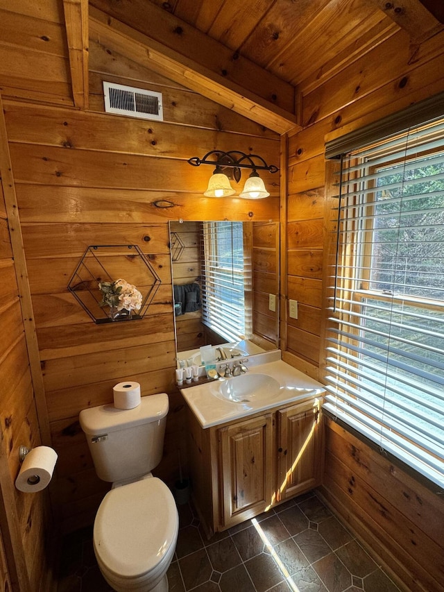 half bathroom featuring lofted ceiling, visible vents, toilet, wood walls, and vanity