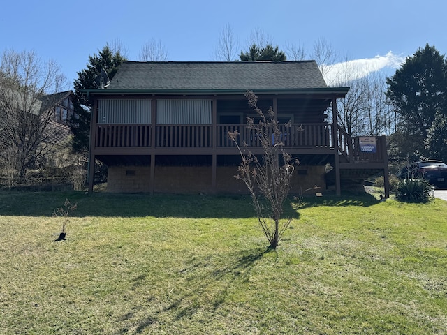 rear view of house with a shingled roof, a deck, and a lawn