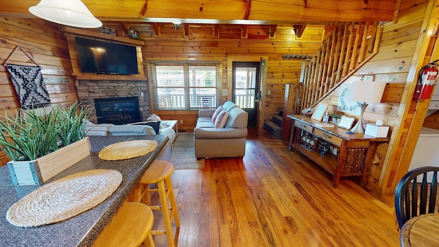 living area featuring a stone fireplace, wood walls, stairs, and hardwood / wood-style floors
