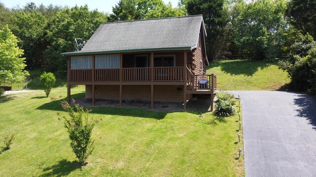 log cabin featuring a shingled roof, a front lawn, a wooden deck, and log exterior