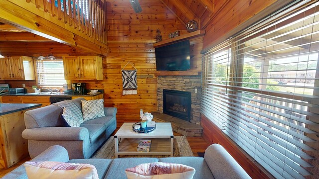 living area featuring a stone fireplace, wood walls, light wood finished floors, and lofted ceiling