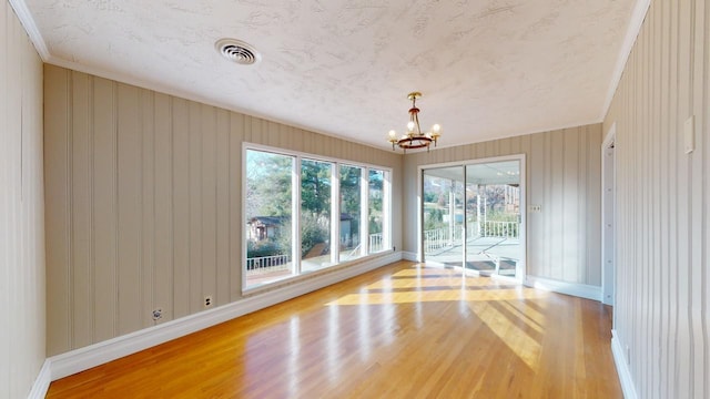 empty room featuring a chandelier, light wood-type flooring, and crown molding