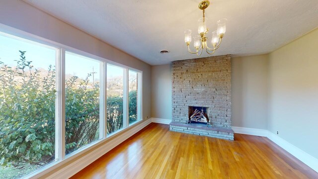 unfurnished living room featuring hardwood / wood-style floors, a brick fireplace, and a notable chandelier