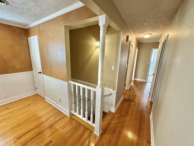 hallway with hardwood / wood-style flooring, ornamental molding, and a textured ceiling