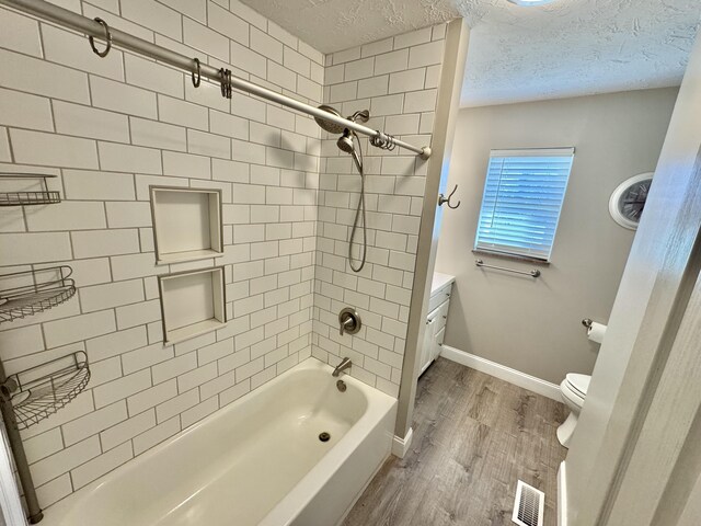 full bathroom with tiled shower / bath combo, hardwood / wood-style floors, a textured ceiling, toilet, and vanity