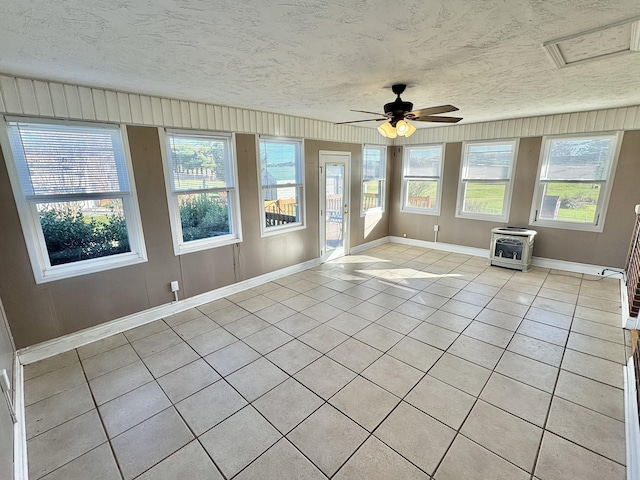 unfurnished sunroom featuring heating unit, ceiling fan, plenty of natural light, and a wood stove